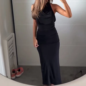 Svart långklänning med öppen rygg - Supersnygg svart långklänning med hög hals och öppen rygg. Klänningen har en tight passform och är ärmlös, vilket ger en elegant och stilren look. Aldrig använd!💓