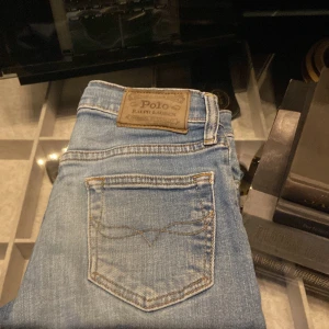 Polo Ralph Lauren The Sullivan Slim jeans - Snygga blå jeans från Polo Ralph Lauren, modell The Sullivan Slim. Jeansen har klassisk femficksdesign, läderpatch bak och diskreta slitningar framtill. Slim passform och tillverkade i mjukt bomullsjeansmaterial. Perfekta för en stilren och avslappnad look.