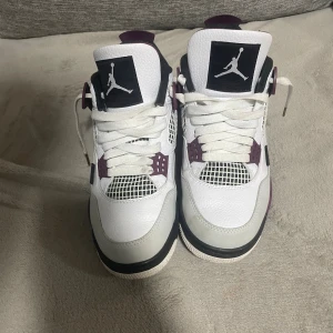 Nike Air Jordan 4 PSG vit vinröd - Kvalitet: Mycket bra, använd ett par gånger men i mycket bra skick.                               Storlek: 41                                                     Nike Air Jordan 4 PSG sneakers i vitt och vinrött med svarta detaljer. Skorna har snörning, meshpaneler och Paris Saint-Germain logga på hälen. Ovandel i skinn och syntet, platt sula och rund tå. Insidan har texten 'ICI C'EST PARIS' och tungan är vinröd med Air Jordan-märke.