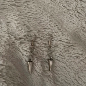 Silvriga örhängen med konform - Säljer ett par coola silvriga örhängen med hängande konformade detaljer. Örhängena har flera små ringar som kedja och spetsiga hängen längst ner. Perfekta för dig som gillar en edgy stil.