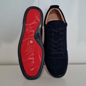 Christian paris marinblå skor - Snygga marinblå sneakers från Christian paris i mocka med klassisk röd sula och broderad logga på hälen. Skorna har rund tå, platt sula och snörning. Perfekta för dig som vill sticka ut med exklusiv design och lyxiga material.