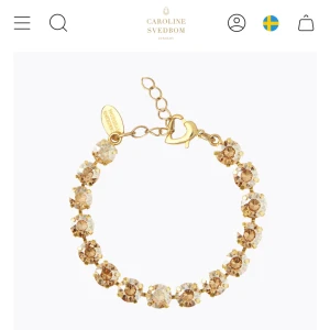 Guldarmband med kristaller Svedbom - Exklusivt armband från Caroline Svedbom med gnistrande ljusbruna kristaller infattade i guldfärgad metall. Justerbar längd med hjärtformad låsdetalj och märkesskylt. Perfekt för dig som vill ha något som verkligen glittrar.