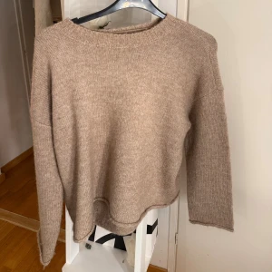 Beige stickad tröja från Vero Moda - Mysig beige stickad tröja från Vero Moda i storlek XS. Tröjan har en avslappnad passform, rund halsringning och långa ärmar. Snygga detaljer på armar och vid kanten på tröjan. Den har ett väldigt skönt material och är aldrig använd.