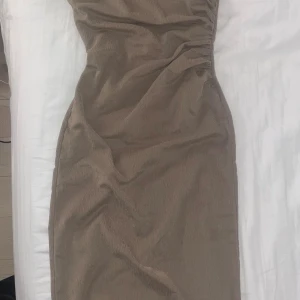 Beige långklänning i manchester - Säljer en beige långklänning i mjukt manchestertyg med figurnära passform. Klänningen har en enkel design utan ärmar och snygga rynkdetaljer på sidan som ger en cool siluett. Perfekt för dig som gillar stilrena och trendiga plagg.