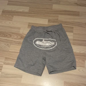 Corteiz shorts - Grå shorts i mjukt material med snörning i midjan och ett vitt tryck av en båt framtill. Perfekta för chill dagar eller träning. Klassisk passform och enkel design som funkar till det mesta.