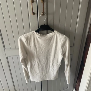 Vit långärmad tröja från Levi's - Vit långärmad tröja från Levi's med klassisk rund hals och liten röd logotyp på bröstet. Enkel och stilren design i mjuk bomull, perfekt till jeans eller kjol. Snygg basic som funkar året runt.