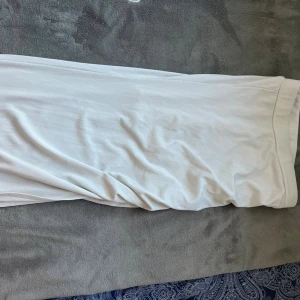 Vit långkjol i mjukt tyg - En stilren vit långkjol med rak passform och bred linning. Kjolen är tillverkad i ett mjukt, lätt material som faller snyggt längs kroppen. Perfekt för dig som gillar minimalistisk och clean stil.