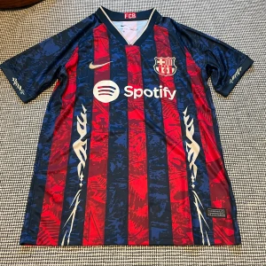 FC Barcelona Nike matchtröja blå/röd - FC Barcelona matchtröja från Nike med klassiska blå och röda vertikala ränder, klubbmärke på bröstet och Spotify-logga. Tillverkad i lätt och ventilerande Dri-FIT-material, kortärmad med V-ringning och gulddetaljer.