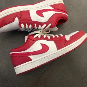 Nike Air Jordan 1 Low röd/vit - Nike Air Jordan 1 Low sneakers i rött och vitt skinn med klassisk swoosh på sidorna. Lågt skaft, perforerad tå och vit mellansula. Röd yttersula och snörning framtill. Perfekta för dig som vill sticka ut med en ikonisk streetstyle.