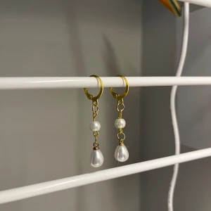 Guldiga örhängen med pärlor - Snygga örhängen med guldfärgade ringar och hängande vita pärlor i två olika former. Perfekt för dig som gillar stilrena smycken med en elegant touch. De har en droppformad pärla längst ner och en rund pärla ovanför. Handgjort