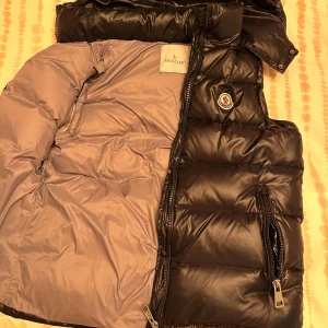 Svart Moncler pufferjacka, stl S - Säljer en svart pufferjacka från Moncler i storlek S. Jackan har glansig finish, klassisk Moncler-logga på bröstet och dragkedjor på fickorna. Insidan är ljusgrå och jackan är vadderad för extra värme. Perfekt för kalla dagar och riktigt snygg streetstil.