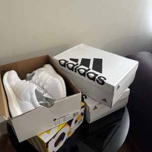 Adidas Ultraboost 1.0 Triple White - Säljer ett par Adidas Ultraboost 1.0 i helvitt. Skorna har stickad ovandel i syntet, klassiska tre ränder på sidan och en boost-mellansula för maxad komfort. Yttersulan är svart med gröna detaljer undertill. Perfekta sneakers för dig som gillar stilren och sportig look. Finns i storlek 43