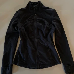 Svart define jacket från Lululemon - Snygg svart define jacket från Lululemon med figurnära passform, hel dragkedja och fickor med dragkedja. Jackan har hög krage och långa ärmar, perfekt för aktiva dagar eller chill vardagsstil. Helt ny oanvänd men säljer då jag beställde fel storlek! Köpte för 1380kr och säljer för nästan samma då den är ny. Kan diskutera pris eller byta mot en liknande fast storlek XS (denna är runt S/M).