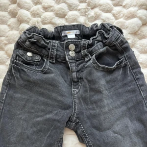 Grå jeans med rynkad midja Gina Tricot - Snygga grå jeans från Gina Tricot med rynkad, elastisk midja och dubbla knappar framtill. Klassisk femficksmodell med raka ben och cool tvättad look. Perfekta för dig som gillar en avslappnad men trendig stil.