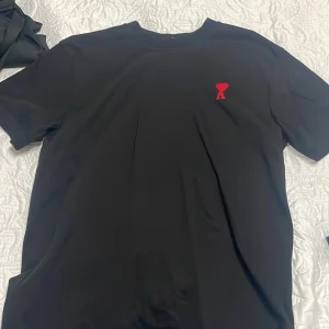 Äkta svart ami paris t shirt. - Svart t-shirt från AMI med klassisk passform och korta ärmar. På bröstet finns ett broderat rött hjärta med bokstaven A. Materialet känns mjukt och är troligen bomull. Diskret AMI-broderi i nacken. Perfekt för en clean och stilren look.