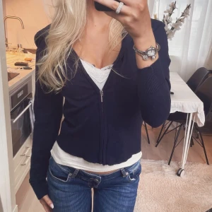 Mörkblå croppad kofta med dragkedja - Snygg mörkblå croppad kofta med dragkedja framtill. Modellen är figurnära med långa ärmar och ribbade muddar. Perfekt att slänga över ett linne eller topp för en chill och stilren look.