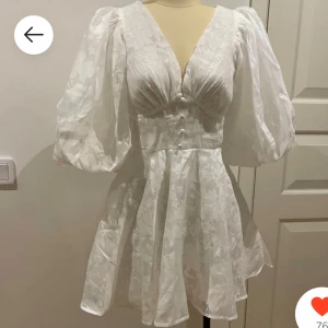 Vit kortklänning med puffärmar - Intressekoll Superfin vit kortklänning med djup v-ringning, markerad midja och stora puffärmar. Klänningen har knappar framtill och ett subtilt blommigt mönster i tyget. Perfekt för dig som vill sticka ut med en romantisk och trendig look. Slutsåld när jag köpte från hemsidan! Perfekt för student. Endast använd en gång. Nypris 1200