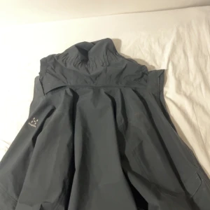 Svart regnjacka från Haglöfs med huva - Snygg svart regnjacka från Haglöfs med huva och dragkedja framtill. Jackan har meshfoder på insidan för extra ventilation och klassisk logga på bröstet. Perfekt för blöta dagar och outdoor-äventyr. Nypris 1500kr, mitt pris 500kr.