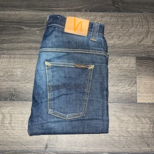 Nudie jeans - Snygga mörkblå jeans från Nudie Jeans i modellen Thin Finn. Klassisk femficksdesign, kontrastsömmar och läderpatch bak. Jeansen är tillverkade i bomull och har en tight passform med smala ben. Perfekta för dig som gillar en stilren och modern look. Midja 39cm, längd 107cm. Ifall det inte finns någon bild i annonsen där jag bär plaggen jag säljer så är det för att jag ej kan ha storleken heller passformen, så kolla måtten för storlek och googla på modellnamnet för passform 😉S2