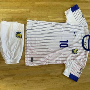 Frankrike Mbappé fotbollströja Nike - Säljer en fransk landslagströja från Nike med Mbappé och nummer 10. Tröjan är vit med tunna blå och röda ränder, blå detaljer vid krage och ärmslut samt landslagsemblem och EM 2020-logga. Matchande vita shorts med emblem ingår. Materialet är lätt och andas.