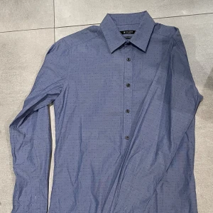 Tiger Of Sweden skjorta - Snygg blå skjorta från Tiger of Sweden med diskret prickigt mönster. Slim fit-modell som är väldigt stretchig med klassisk krage och svarta knappar framtill. Långärmad och tillverkad i mjuk bomull som känns skön mot huden. Perfekt för dig som gillar stilrena detaljer och för dig som vill ha den fetaste outfiten i skolan eller på fest. Storlek M (slim fit) och passar mig som är ungefär 185! Skicket är bra och finns knappt några tecken på användning! Hör av dig vid minsta lilla mvh EM_resell