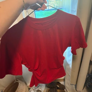 Röd t-shirt - Säljer en röd figursydd t-shirt med korta ärmar och rund hals. Toppen har en snygg slits på baksidan som ger en cool och trendig look. Perfekt för dig som gillar färg och vill sticka ut lite extra. Materialet känns mjukt och skönt mot huden.