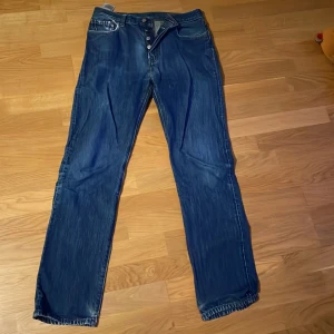 Levi's 501 blå jeans W27 L32 - Klassiska Levi's 501 jeans i blå denim med raka ben och knappgylf. Snyggt slitna detaljer och ikoniska bakfickor med Levi's röda etikett. Modellen är straight fit och passar dig som gillar en tidlös look. Perfekta till sneakers eller boots.