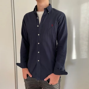 Mörkblå skjorta från Ralph Lauren - Mörkblå skjorta från Ralph Lauren i slim fit med klassisk röd broderad logga på bröstet. Skjortan är stilren och passar till alla årstider✅🤩 endast använd ungefär vid två tillfällen så nästintill helt ny💯nypriss 1200kr mitt pris 449kr priset är självklart inte hugget i sten🪨 och det är bara att skriva om du har några funderingar svarar snabbt✅
