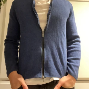 Marinblå kofta från Massimo Dutti - Snygg marinblå kofta från Massimo Dutti med stilren design och hel dragkedja framtill. Tröjan är stickad i mjukt material och har långärmad passform med ribbad krage. Perfekt för dig som gillar klassisk och enkel stil.