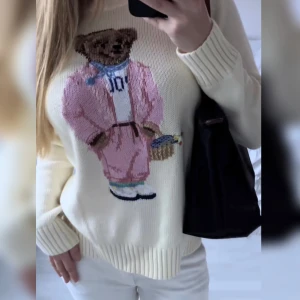 Ralph Lauren - Vit stickad tröja från Polo Ralph Lauren med ikoniska Polo Bear-motivet framtill. Björnen har rosa outfit, blå scarf och sneakers. Tröjan har rund halsringning, ribbade muddar och avslut. Köpt på Vinted för 1 år sedan 