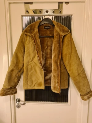 Beige pälsjacka från Naf Naf - Säljer en beige pälsjacka från Naf Naf med mjuk fuskpäls på insidan och krage. Jackan har dragkedja och långa ärmar med pälsdetaljer vid mudden. Utsidan är gjord av äkta svinskinn och insidan av akryl. Perfekt för kalla dagar! 