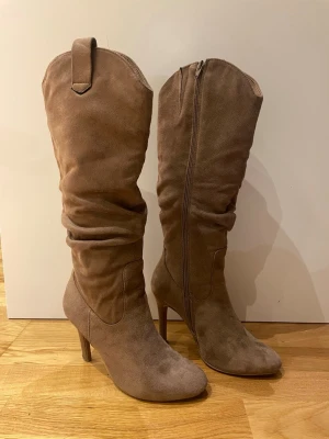 Bruna mockastövlar med klack Anna Field - Snygga bruna stövlar från Anna Field i mjuk mocka med hög klack och rund tå. Stövlarna har en slouchy design och dragkedja på sidan för enkel påtagning. Perfekt för dig som vill ha en chic och trendig look till hösten eller vintern🤗