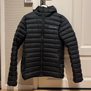 Svart dunjacka Peak Performance  - Svart dunjacka från Peak Performance i storlek M. Jackan har huva, horisontella quiltade paneler och dragkedja framtill. Perfekt för kalla dagar med sin lätta och fluffiga känsla. Jackan är typ ny använd max 5 gånger, säljer pågrund av att den var för liten för mig. Kan fixa fram kvitto om du är intresserad av det. Om inte priset passar testa lägg ett bud, mvh Vidar