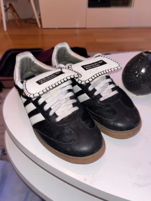 Adidas Samba sneakers svart/vit wales Bonner - Adidas  sneakers i svart och vitt med klassiska tre ränder på sidan, vit plös med svart kantdetalj och gummisula. Skorna har snörning och rund tå, tillverkade i skinn och mocka för en sportig och retro vibe.