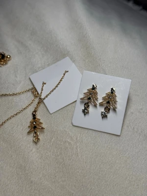 Juligt Gransmyckeset – Halsband & Örhängen - Sött smyckeset i guldton med julgransmotiv. Innehåller halsband och örhängen – båda helt nya. Perfekt som julklapp eller att bära under december.  💰 Nypris: ca 99–149 kr per del (värde ca 200–300 kr totalt).