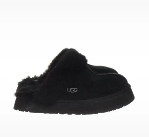 Svarta UGG slip-in boots med päls - Mysiga svarta slip-in boots från UGG med fluffig päls runt öppningen och platt sula. Storlek 39! Skorna har en rund tå och är tillverkade i mocka med mjukt foder, perfekta för kalla dagar. UGG-loggan syns på sidan och sulan har ett mönstrat grepp. Lite slitet i hälen men inget man tänker på :) annars i bra skick!