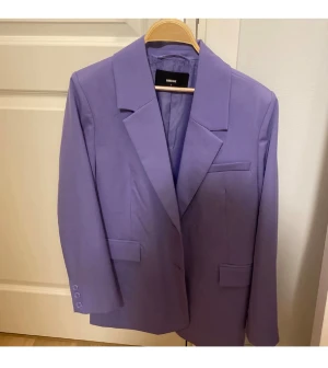 Lila kavaj från Bik Bok - Snygg lila kavaj från Bik Bok med klassisk krage och tre knappar vid ärmslutet. Kavajen har raka linjer, fickor med lock och en bröstficka. Perfekt för dig som vill sticka ut med färg och stil.