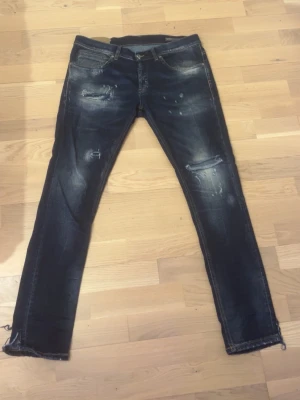 Mörkblå dondup slitningar - Säljer ett par mörkblå jeans från Dondup med coola slitningar och detaljerade sömmar. Jeansen har klassisk femficksdesign, orange broderi på bakfickan och slitna partier både fram och bak för en edgy look. Perfekt för dig som gillar streetstyle.