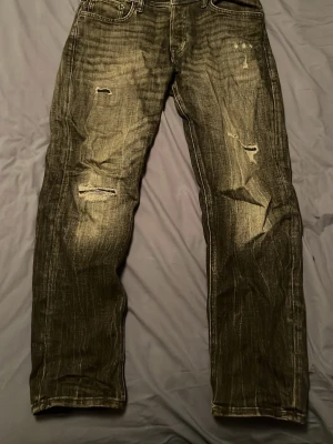 Svarta slitna jeans i straight fit - Svarta jeans med slitningar och trasiga detaljer på benen. Modellen har raka ben och klassisk femficksdesign. Jeansen har en cool tvättad look och är tillverkade i jeansmaterial. Perfekt för dig som gillar streetstyle och vill ha en avslappnad vibe.