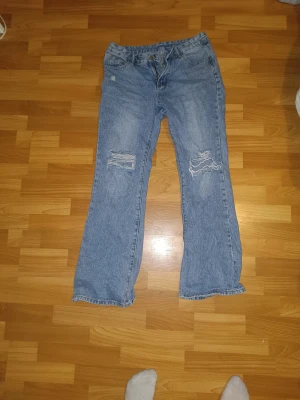 Low rise Blå bootcut jeans med slitna knän ( utsvängda)  - Säljer ett par ljusblå jeans med bootcut passform och slitna detaljer vid knäna. Klassisk femficksmodell med dragkedjah knapp framtill. Jeansen  är tillverkade i jeansmaterial. Perfekt för dig som gillar en avslappnad och trendig look. Dom är low waist och flared 