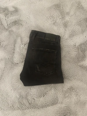Replay Anbass Jeans - Svarta Replay Anbass jeans i slimfit med slitningar. Jeansen är gjorda i stretchigt denim för skön passform och har en modern, smal siluett. Storlek 32/36. 