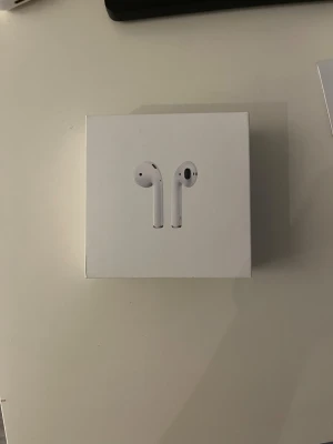 Apple AirPods - Säljer ett par Apple AirPods med laddningsetui, komplett med originalförpackning. Hörlurarna är trådlösa och passar perfekt till både iPhone och andra enheter med Bluetooth. Skick: mycket bra, inga synliga skador eller slitage på etui eller förpackning.
