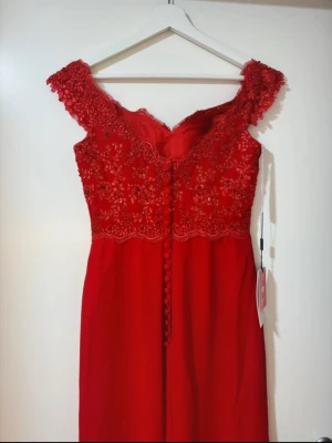 Röd långklänning med spets  - Elegant röd långklänning från JJ’s house med vacker broderad spets. Aldrig använd, strl 34