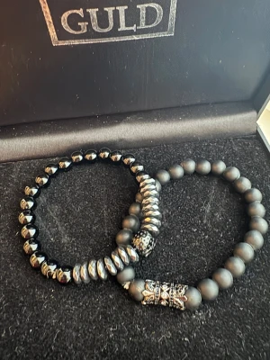 Svarta pärlarmband med döskalle och mönster - Två coola armband , ett med svarta och silverfärgade facetterade pärlor och en döskalle i metall, och ett med matta svarta pärlor och ett detaljerat silverfärgat mönster. Perfekt för dig som gillar edgy och stilrena accessoarer.