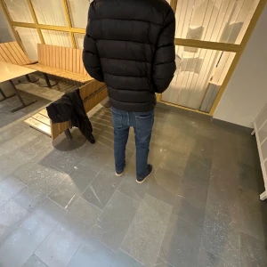 Svart dunjacka från Parajumpers - Säljer en svart dunjacka från Parajumpers med klassisk patch på ärmen och gul detalj vid kragen. Jackan har en quiltad design, dragkedja framtill och hög krage. Perfekt för kalla dagar!