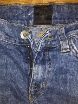 Blå skinny jeans från Tiger of Sweden - Säljer ett par klassiska blå jeans från Tiger of Sweden med skinny passform. Jeansen har fem fickor, dragkedja och knapp framtill samt snygga kontrastsömmar. Perfekta för dig som gillar en smal siluett och stilren look.