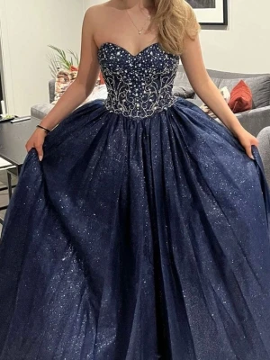 Marinblå glittrig balklänning med snörning - Vacker mörkblå balklänning från Lychinor. Nyligen köpt för 9000 kr. Storlek XXS. Den har snörning bak och kan bäras från storlek XXS-M.  Som referens är jag 165 cm lång och den når marken precis lagom, utan att den hänger.  Kan sys upp eller klippas av för kortare längd.  Endast använd en kväll.