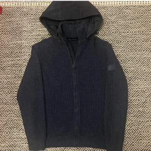 Stickad Cardigan - Säljer en mörkblå stickad cardigan från Polo Club med avtagbar huva , likt trendiga massimo dutti. Inga tecken på användning. Perfekt för kyliga dagar och perfekt att matcha med vit T-shirt och ett par feta jeans😉