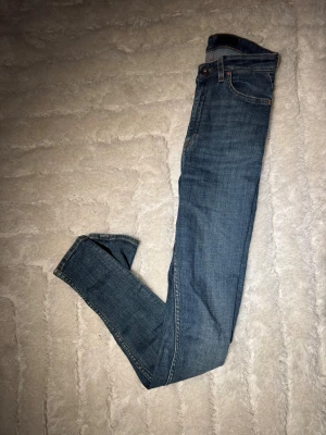 Blå jeans Sandie från Titer Of Sweden - Snygga blå jeans från Tiger Of Sweden, modell Sandie. Klassisk femficksdesign med bruna sömmar och läderpatch bak i midjan. Jeansen har en smal passform och är tillverkade i mjukt denimtyg. Perfekta för dig som gillar stilrena och tidlösa jeans. W 29, L 32