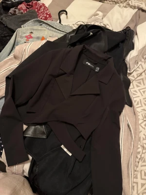 Svart croppad bolerotopp FB Sister XS - Snygg svart croppad bolerotopp från FB Sister i storlek XS. Toppen har djup v-ringning, omlott-design och långa ärmar. Stilren krage och figurnära passform som ger en cool och trendig look. Perfekt för dig som gillar att sticka ut med din outfit.